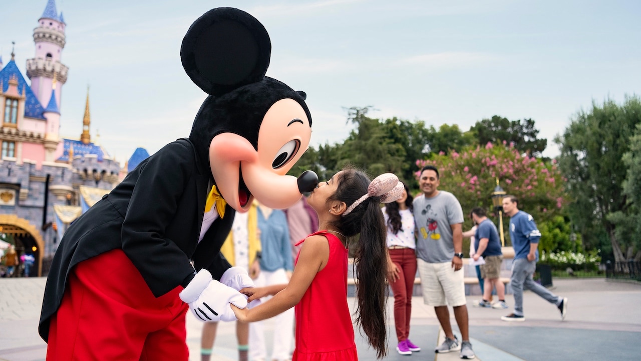 A joyful little girl giving a sweet kiss on Mickey Mouse's nose in front of Sleeping Beauty Castle, filled with magical moments.